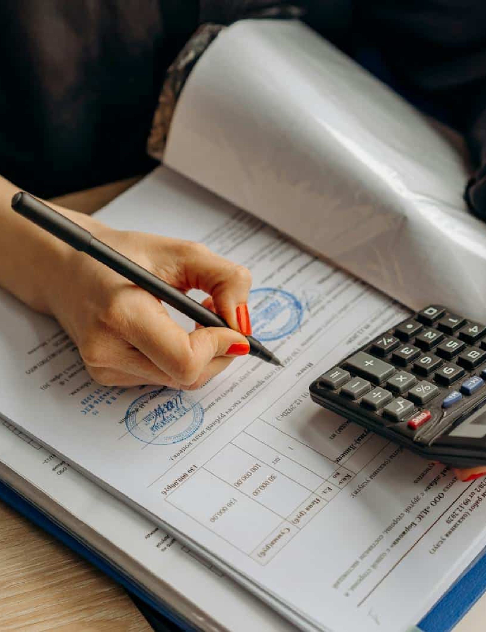 An accountant using a calculator and signing paperwork, showcasing financial analysis.